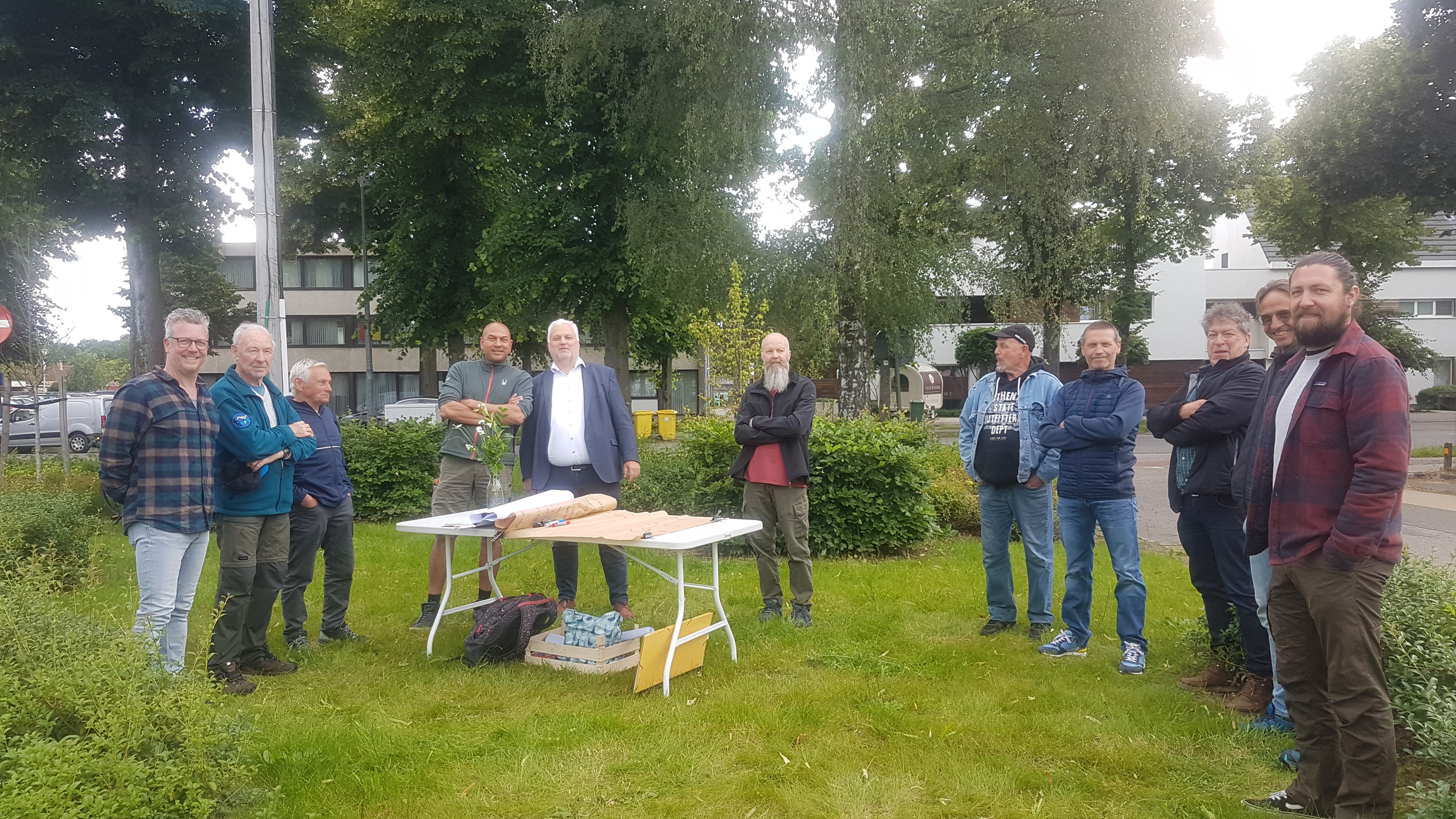 Mensen staan op een graspleintjes rond een tafel met plannen