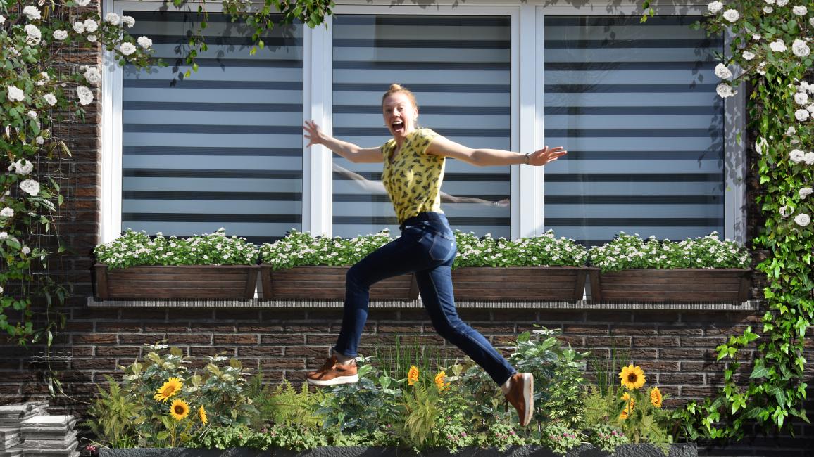 Vrouw springt enthousiast in de lucht voor een groene gevl