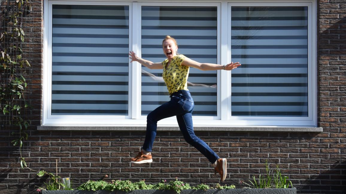 Vrouw springt enthousiast in de lucht voor een gevel zonder begroeiing