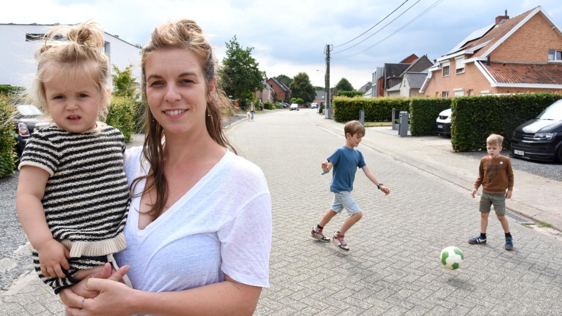 Vrouw met meisje op de arm en twee voetballende jongens op de achtergrond in een grijze straat